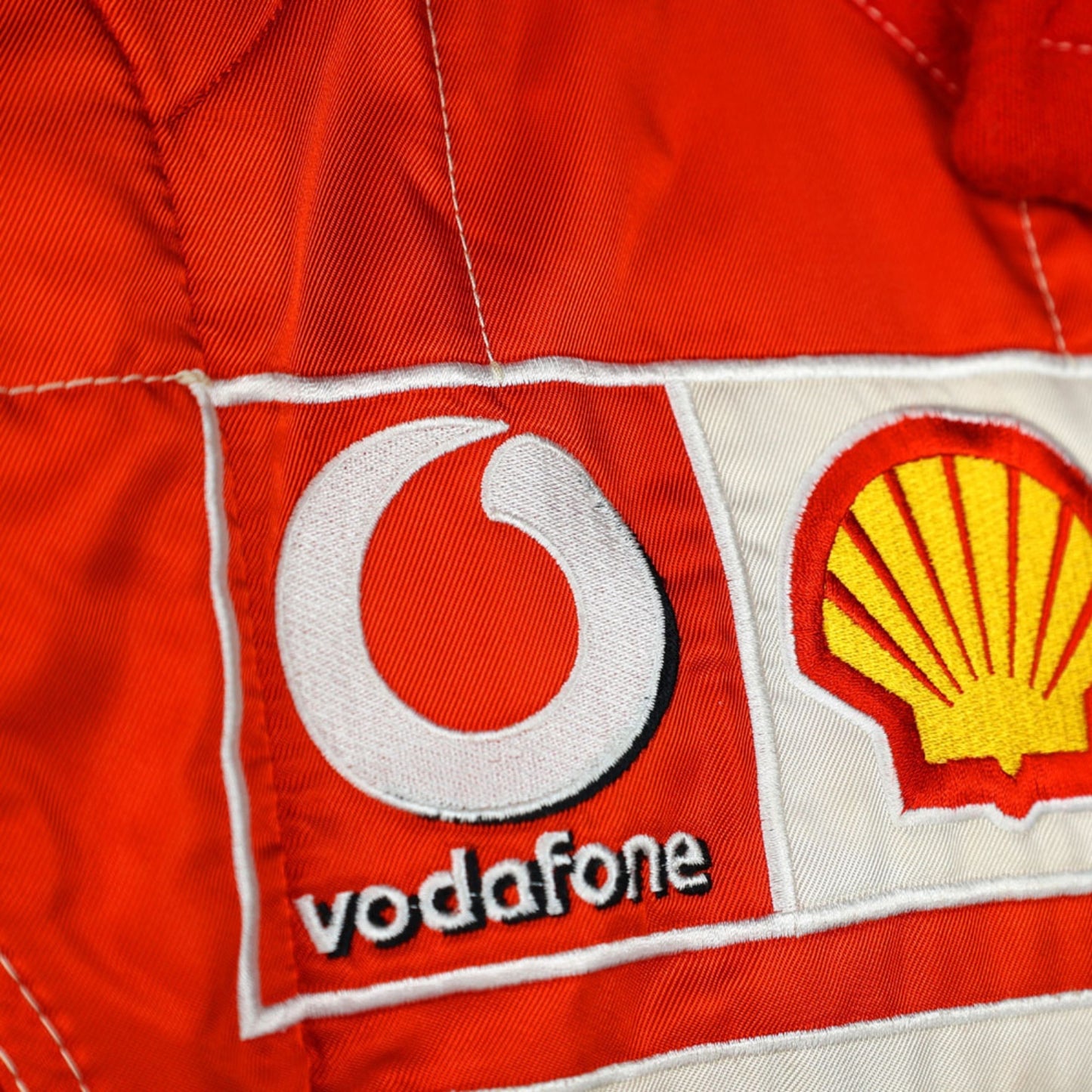 Close-up shot of Schumacher’s 2006 race suit, highlighting the detailed stitching, premium red material, and signature white branding elements.
