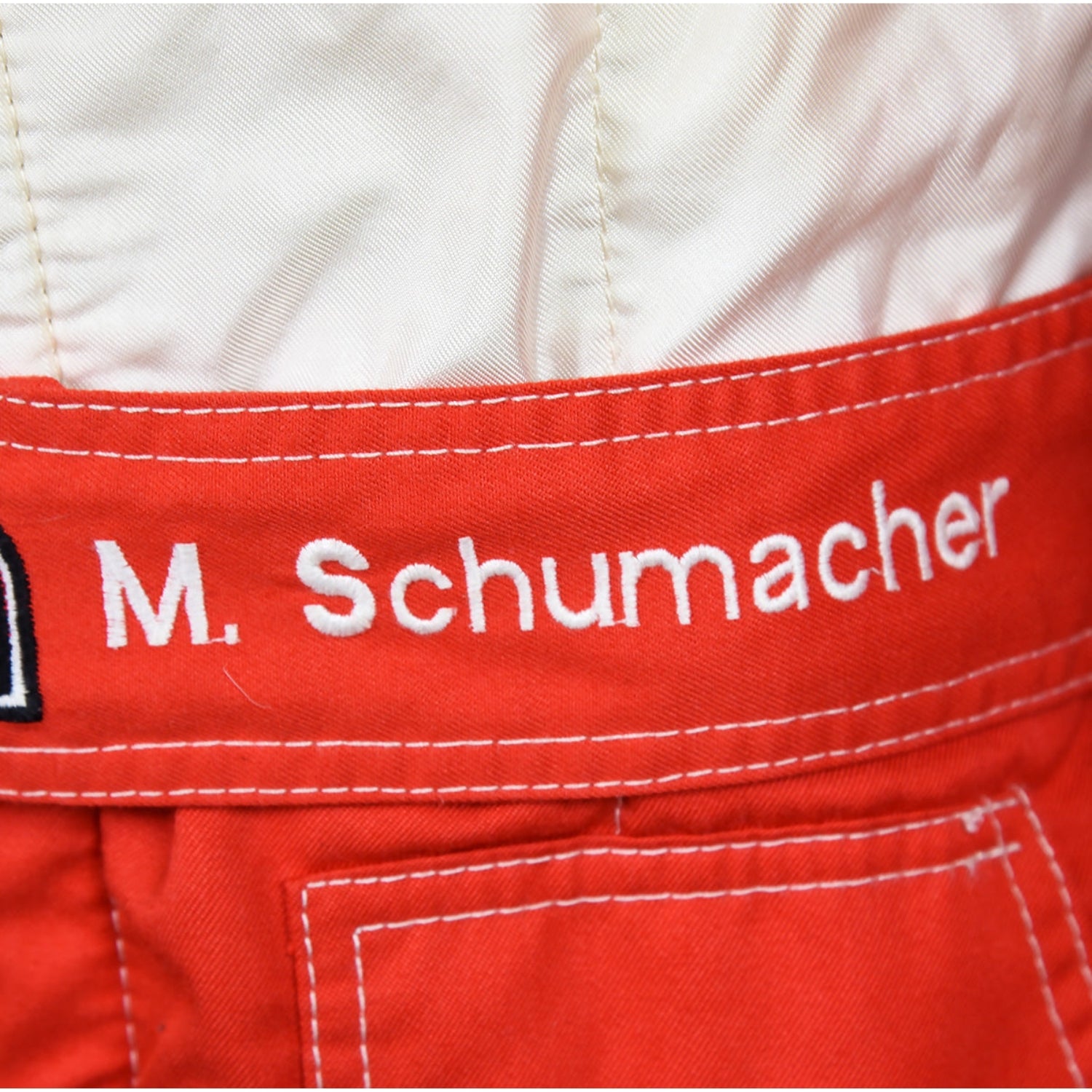 Close-up of Schumacher’s 1997 F1 race suit, displaying detailed stitching and rich red fabric, with sponsor logos highlighting his drive during the 1997 season.