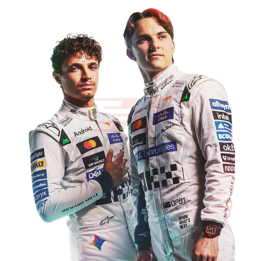 Close up View of Two race drivers Oscar Piastri and Lando Norris in white 2026 McLaren Bristish GP f1 racing suits with sponsor logos, standing against a white background. The suits feature prominent patches and branding including Castore, Alpinestars, and DPPI.