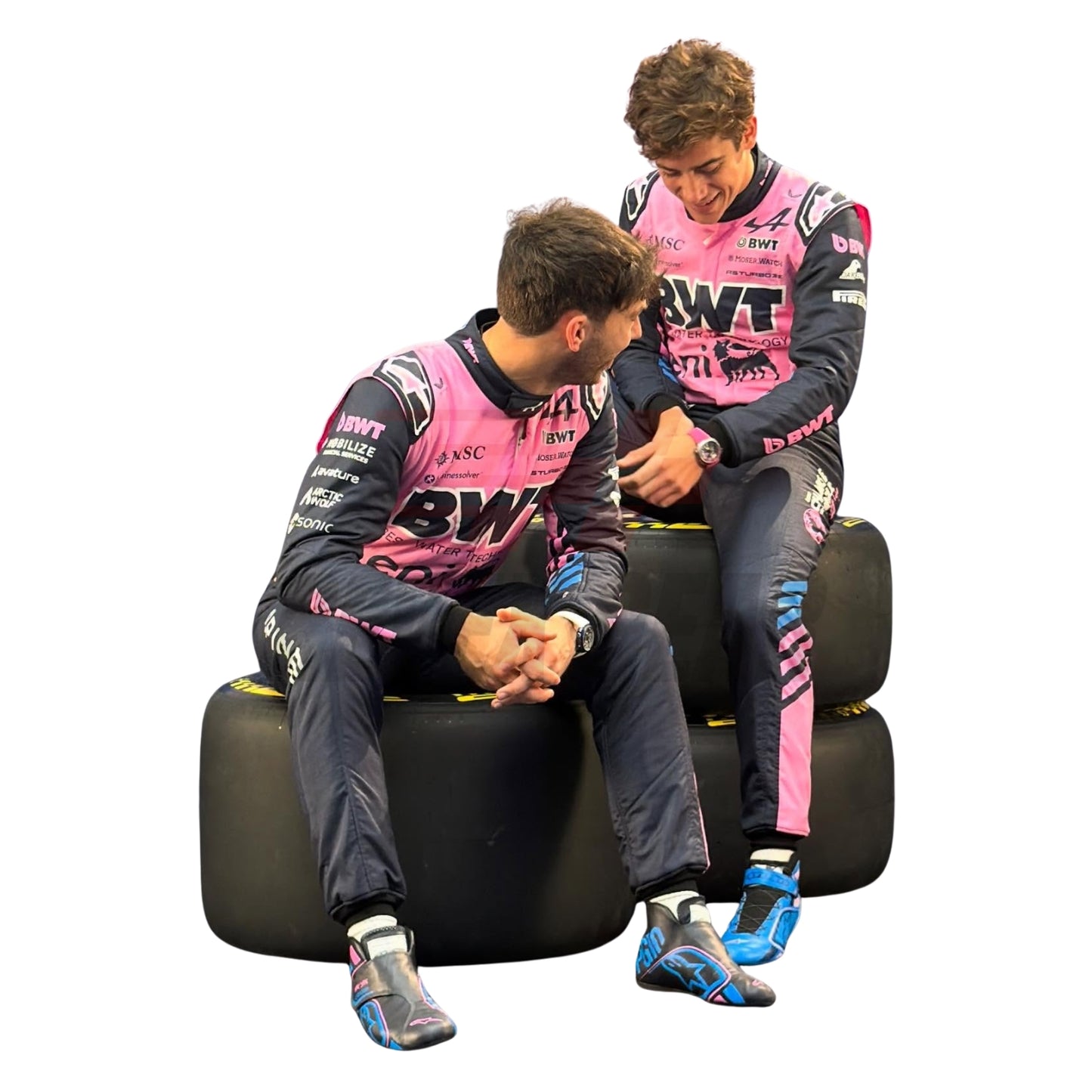 Pierre Gasly and Franco Colapinto in racing suits sitting on racing tires against a white background