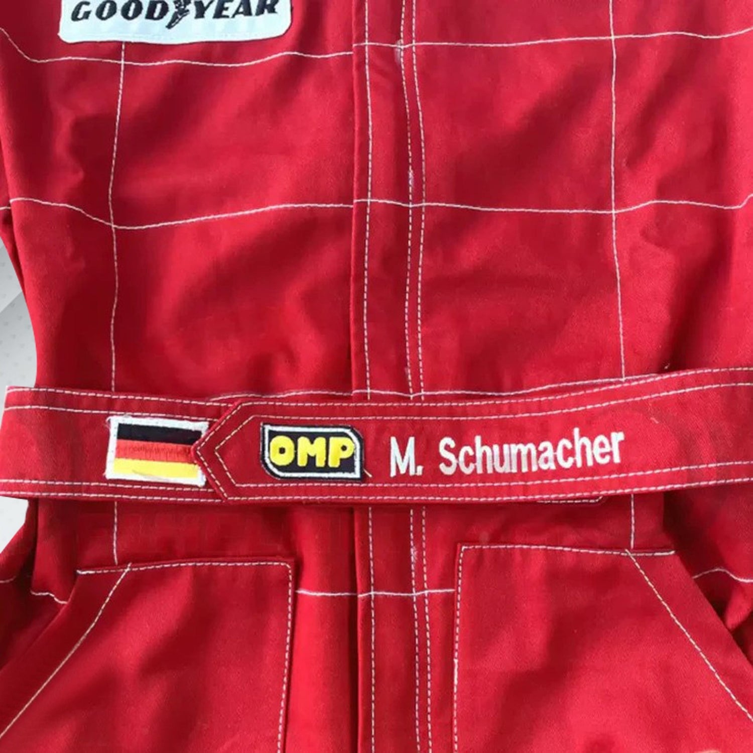 Close-up of Schumacher’s 1996 F1 suit, featuring the detailed stitching, Ferrari red color, and early sponsor branding from his debut season