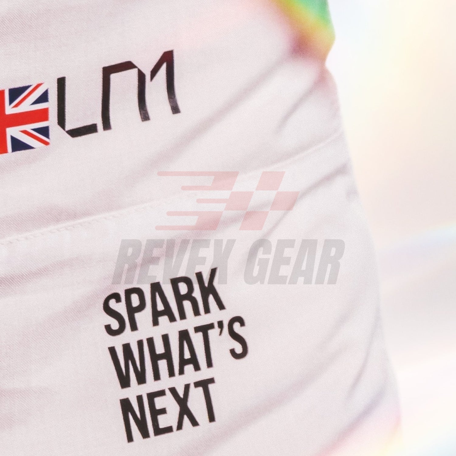 Close-up of a white Lando Norris 2026 British GP F1 Racing suit garment with black printed text reading 'SPARK WHAT'S NEXT' and a Union Jack logo with 'LM1' above it. A faint 'REVEX GEAR' watermark is visible across the center.