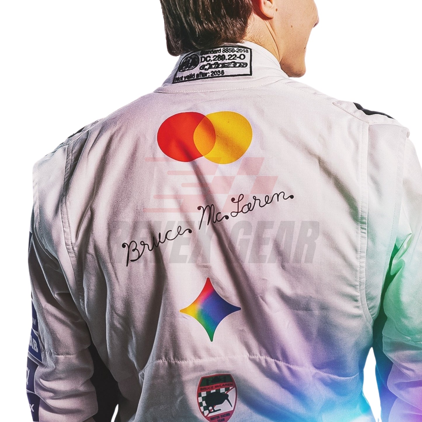 Back view of an Oscar Piastri wearing a white McLaren British GP 2026 F1 racing suit with colorful graphics, including a large red and yellow Mastercard logo, a rainbow star, and 'Bruce McLaren' script, worn by a model.